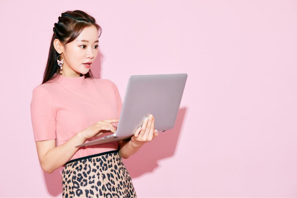 パソコンを見ながら驚く女性　ピンクの背景